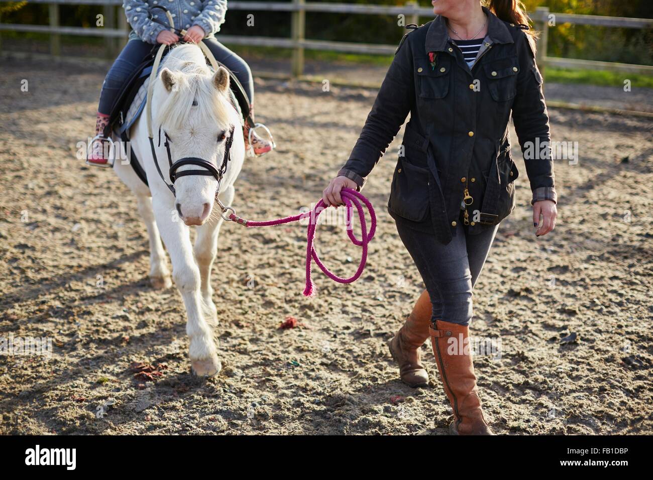 Instructor leading girl learning to ride pony in equestrian arena Stock