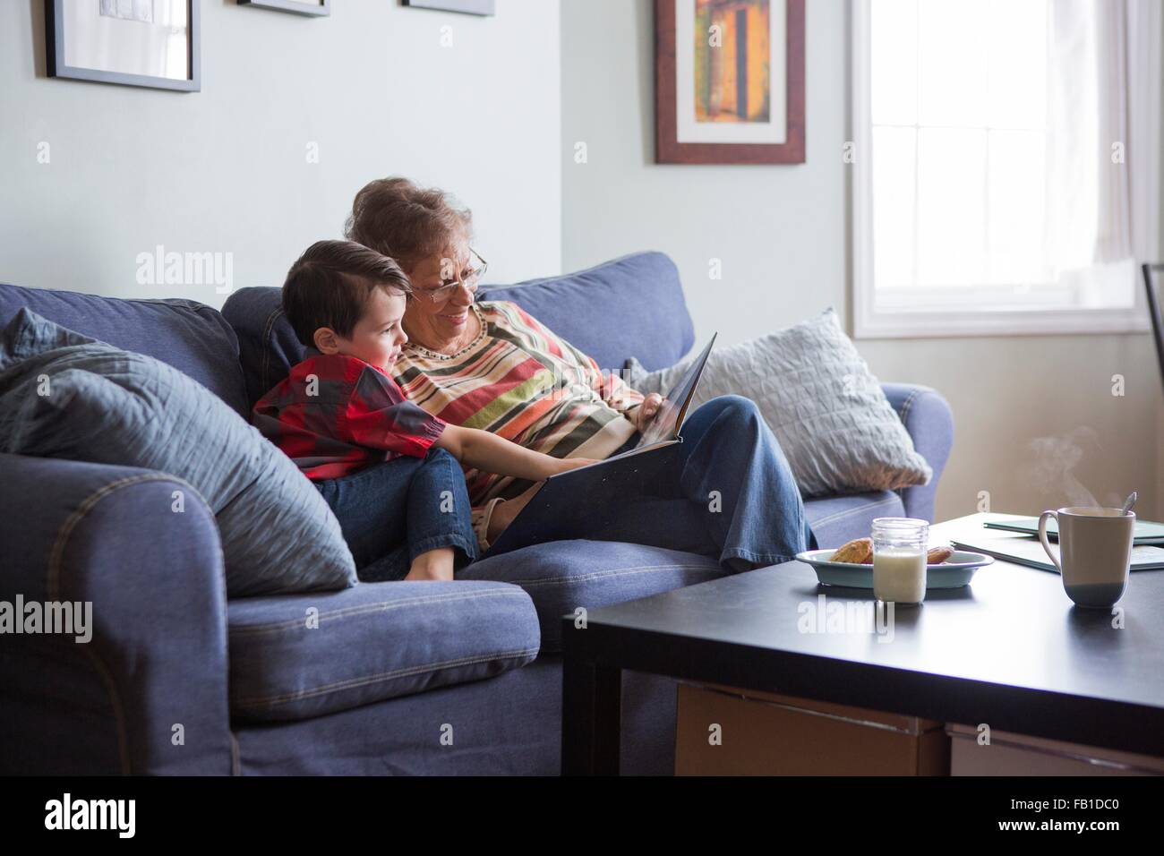 Senior woman reading book with grandson on sofa Stock Photo
