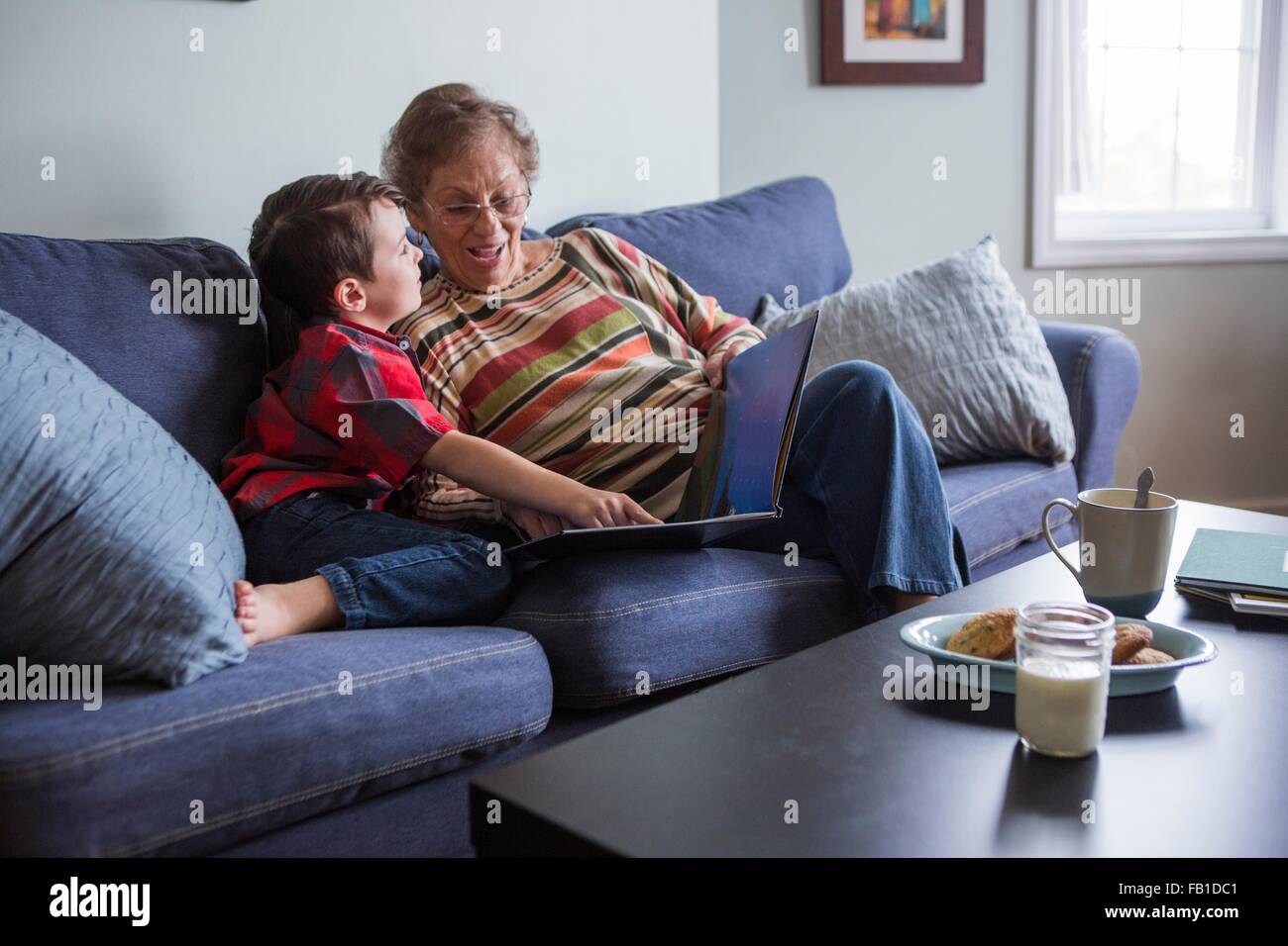 Senior woman explaining book to grandson whilst reading on sofa Stock Photo