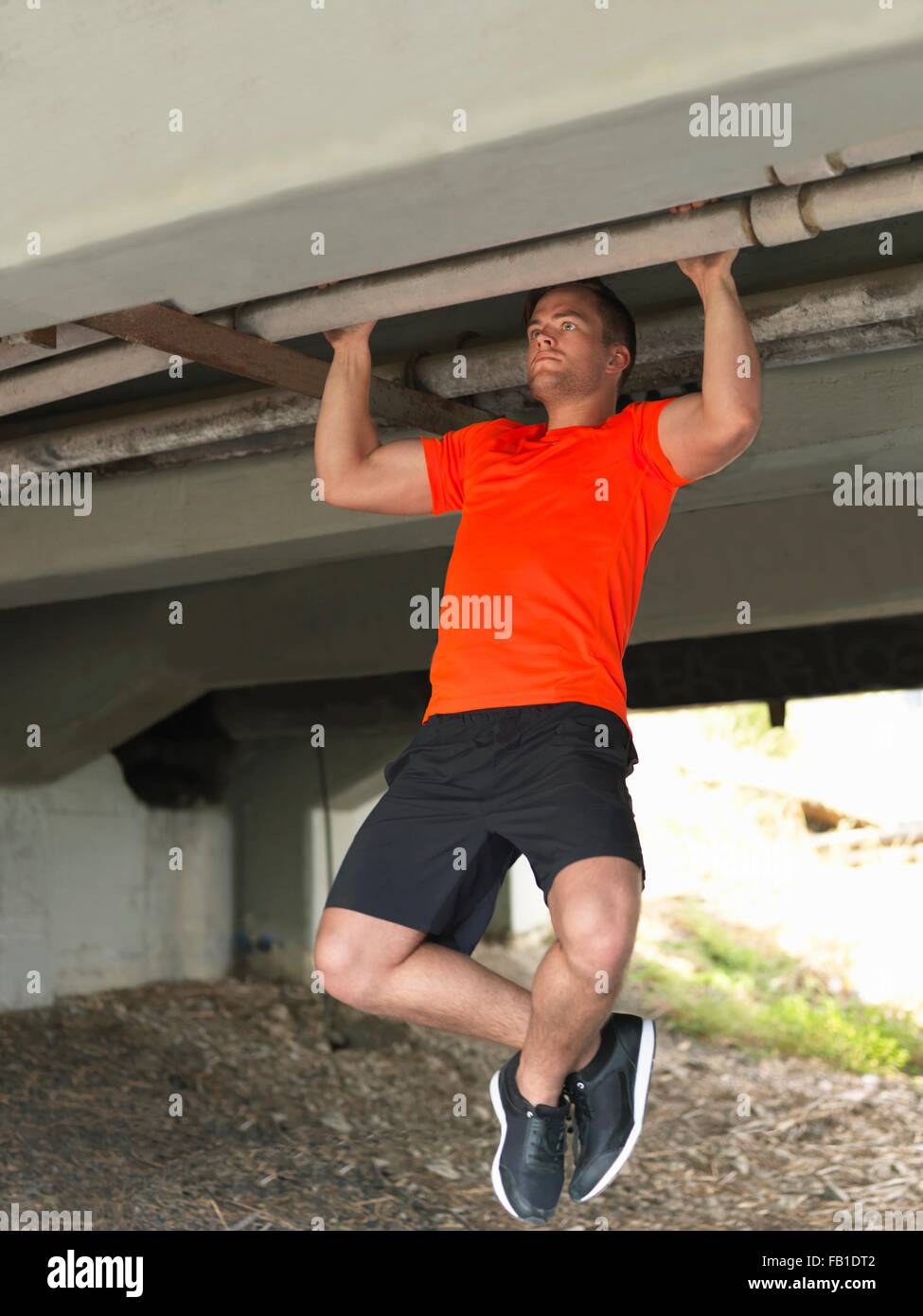 Young man doing pull ups under bridge Stock Photo