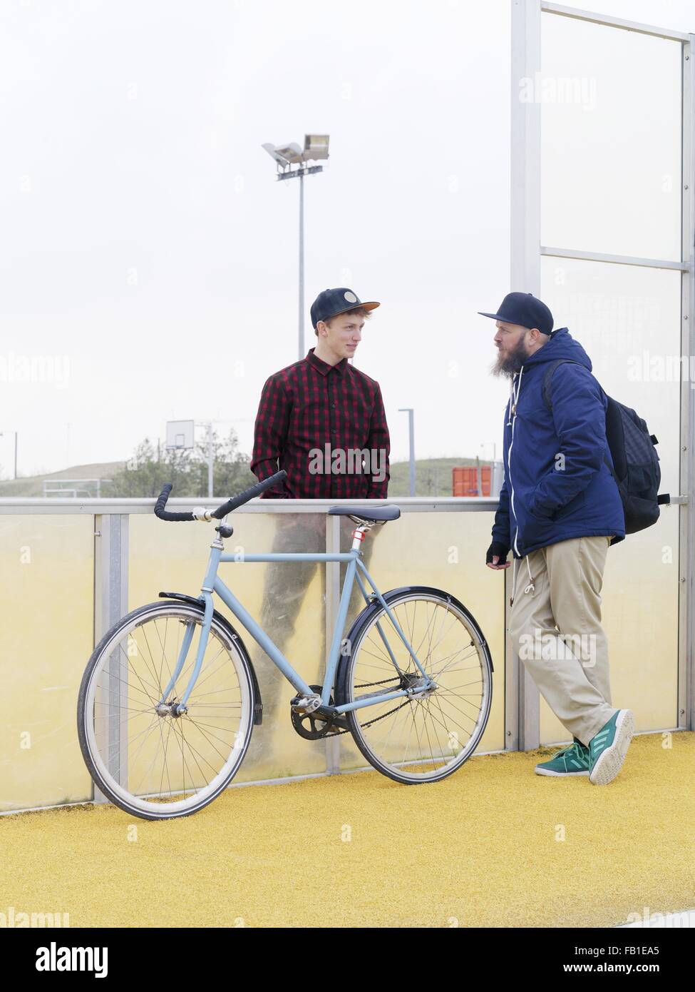 Urban cyclists chatting by fence on sports field Stock Photo