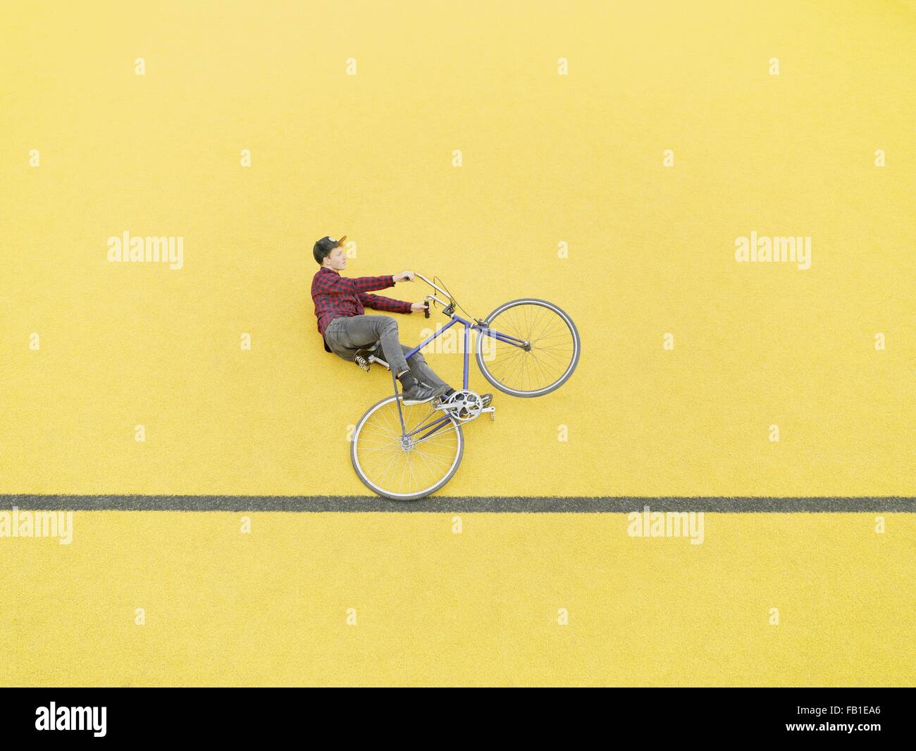 Urban cyclist doing illusionary stunt against yellow wall Stock Photo