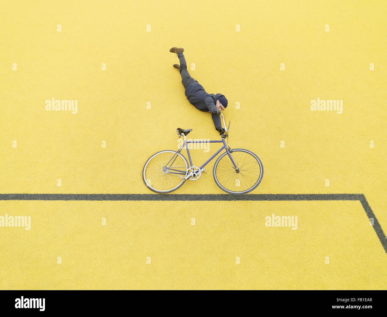 Urban cyclist doing illusionary stunt against yellow wall Stock Photo