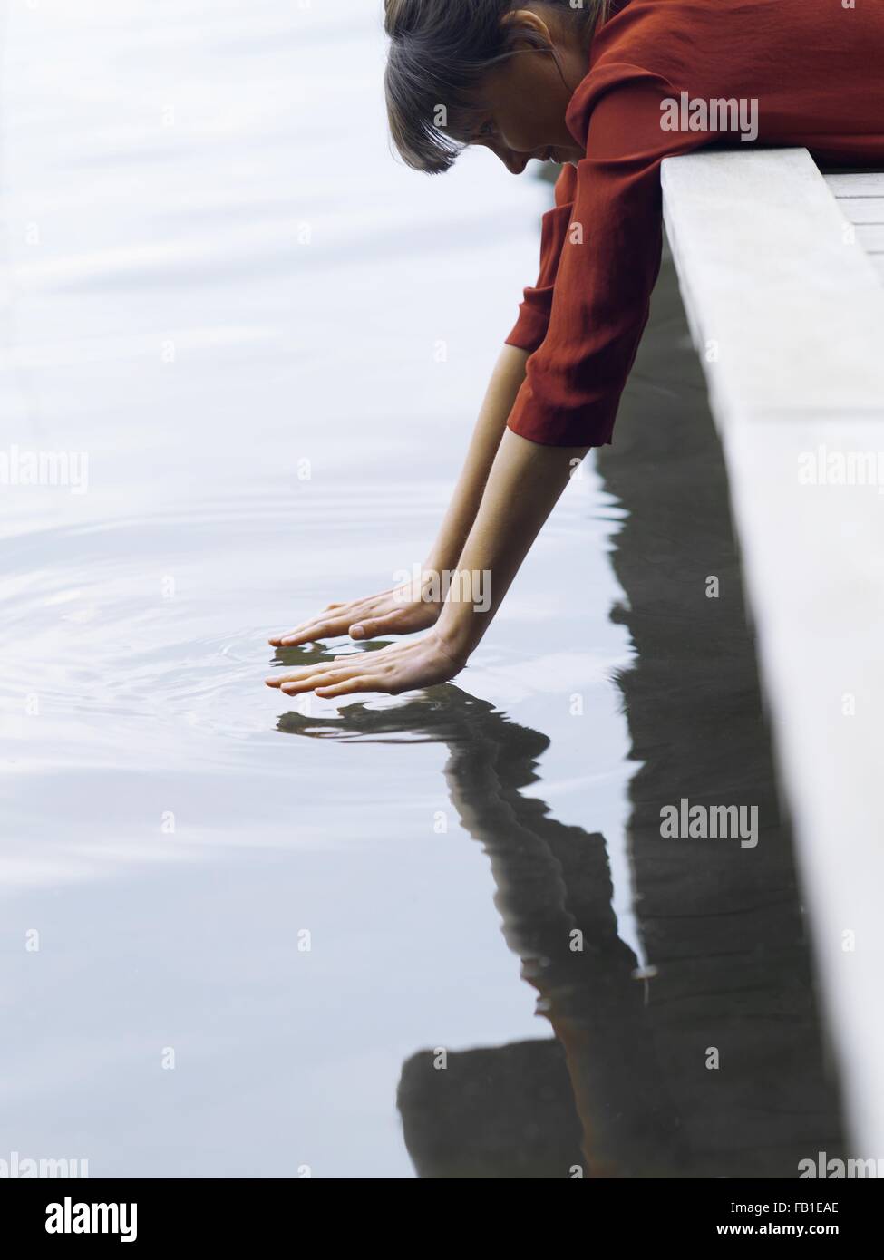 Woman lying on front hanging off pier touching surface of water, Copenhagen, Denmark Stock Photo