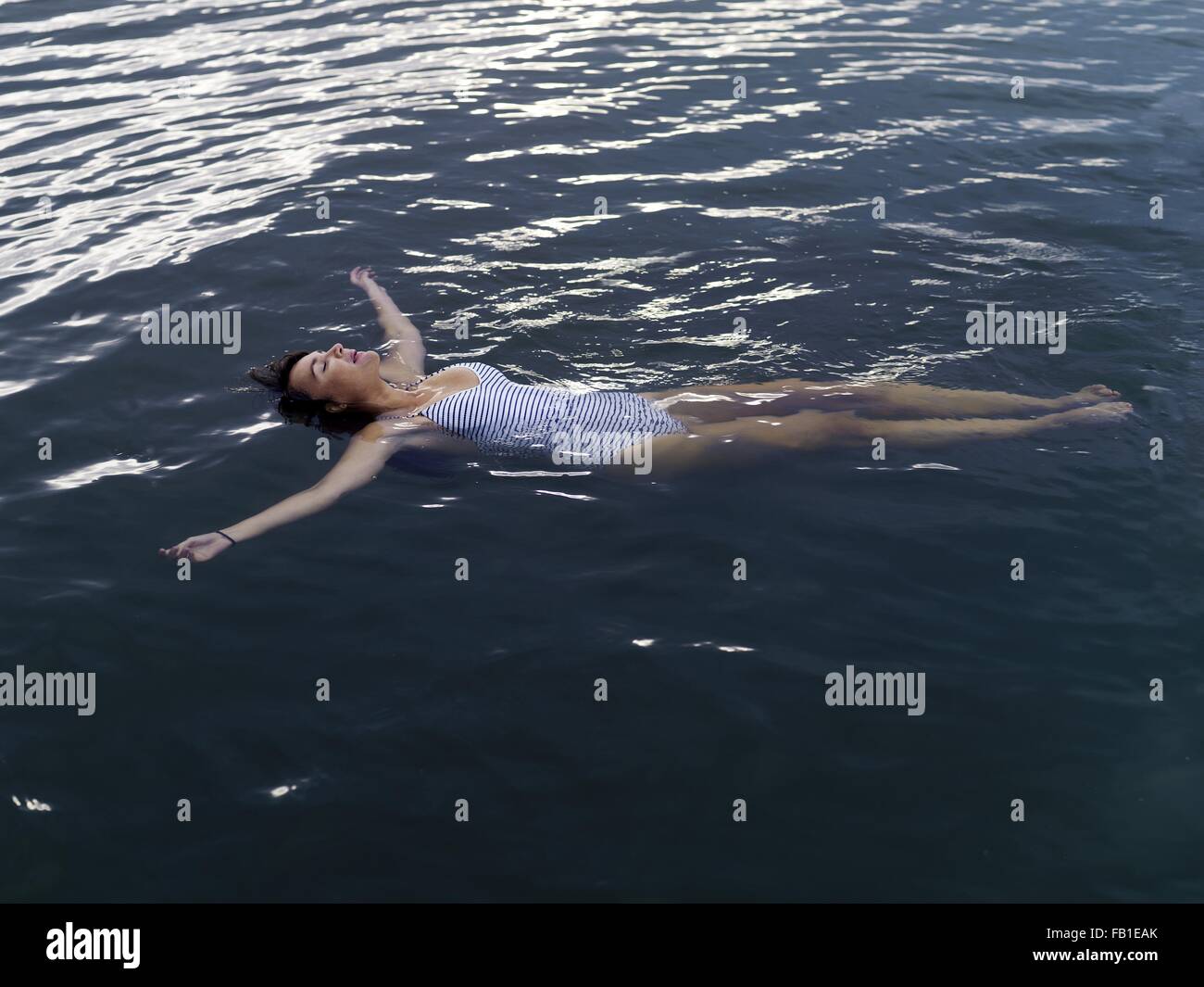 High angle view of woman floating on back in water arms outstretched looking up Stock Photo
