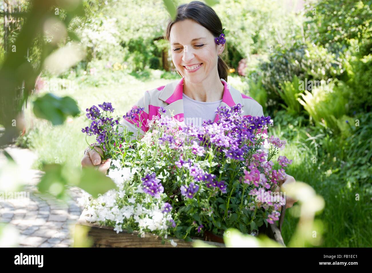 Mature woman carrying wooden crate filled with flowers smiling Stock Photo