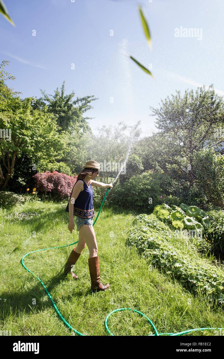 Side view of mature woman in garden squirting water into air with hosepipe Stock Photo