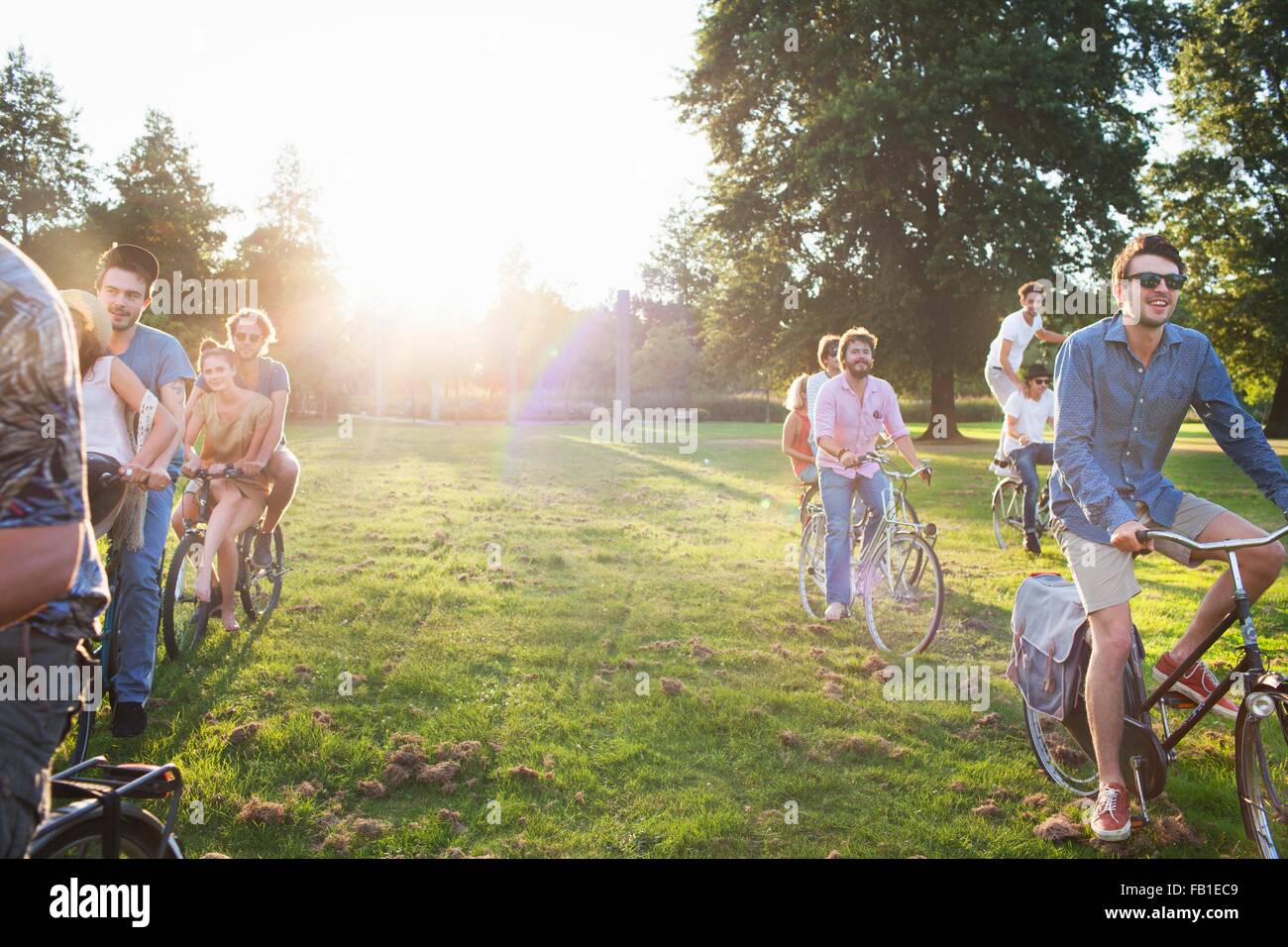 Rows of party going adults arriving in park on bicycles at sunset Stock Photo