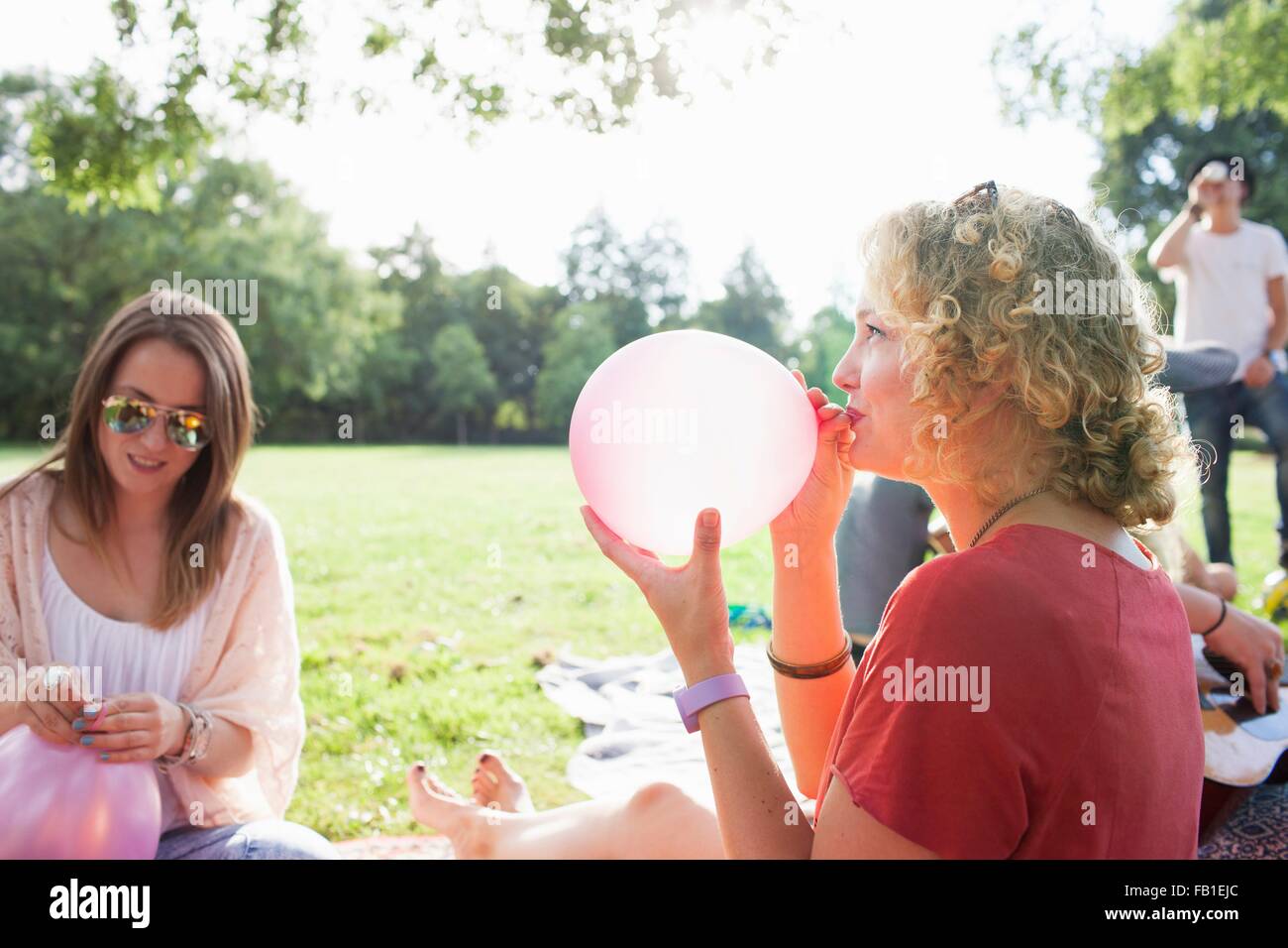 Young woman blowing up balloon at park party Stock Photo