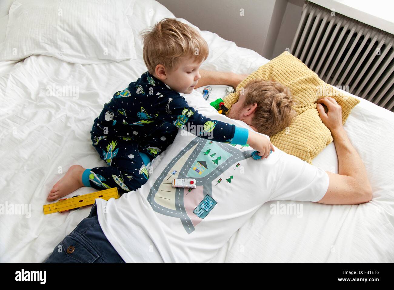 Young boy playing with toy car on back of fathers tshirt in bed Stock Photo