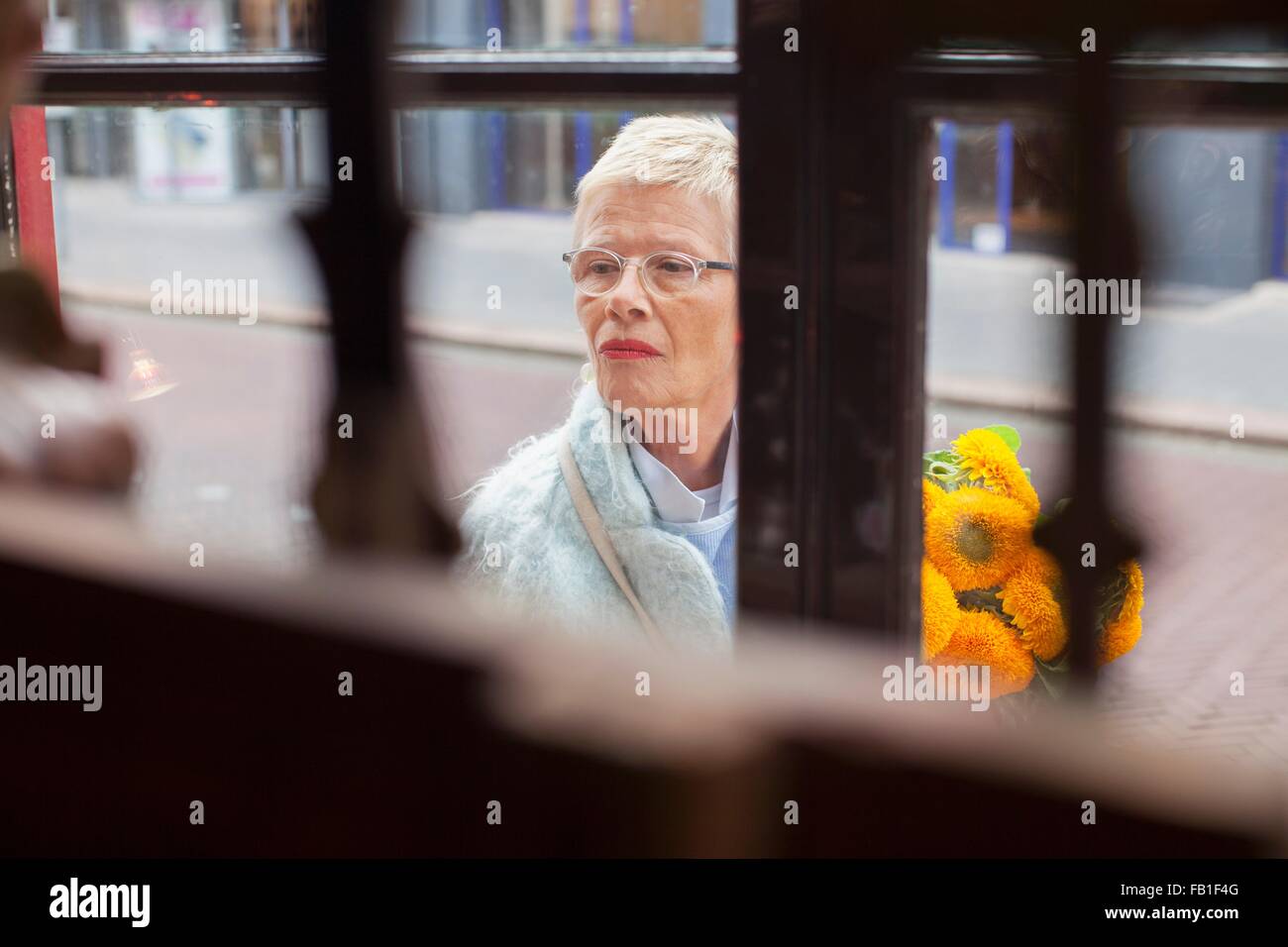 Mature woman with bunch of yellow flowers window shopping Stock Photo