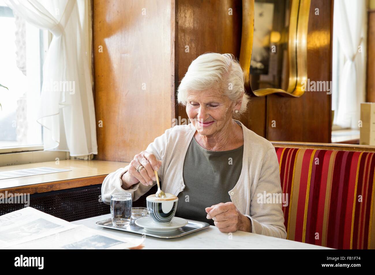 Senior woman sitting in cafe, stirring coffee Stock Photo