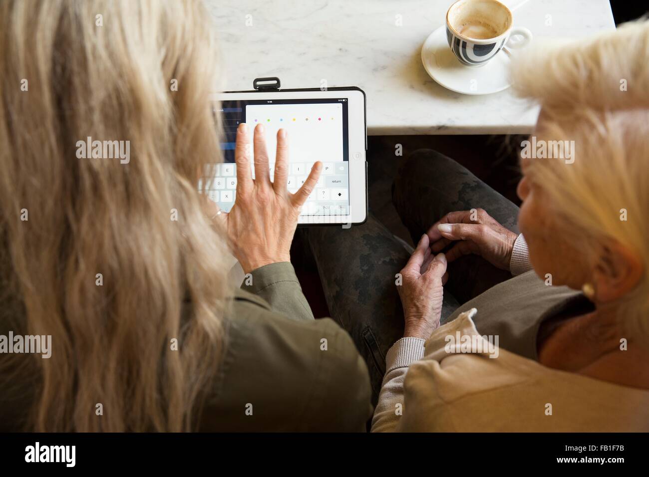 Mother and daughter sitting together in cafe, looking at digital tablet, rear view Stock Photo