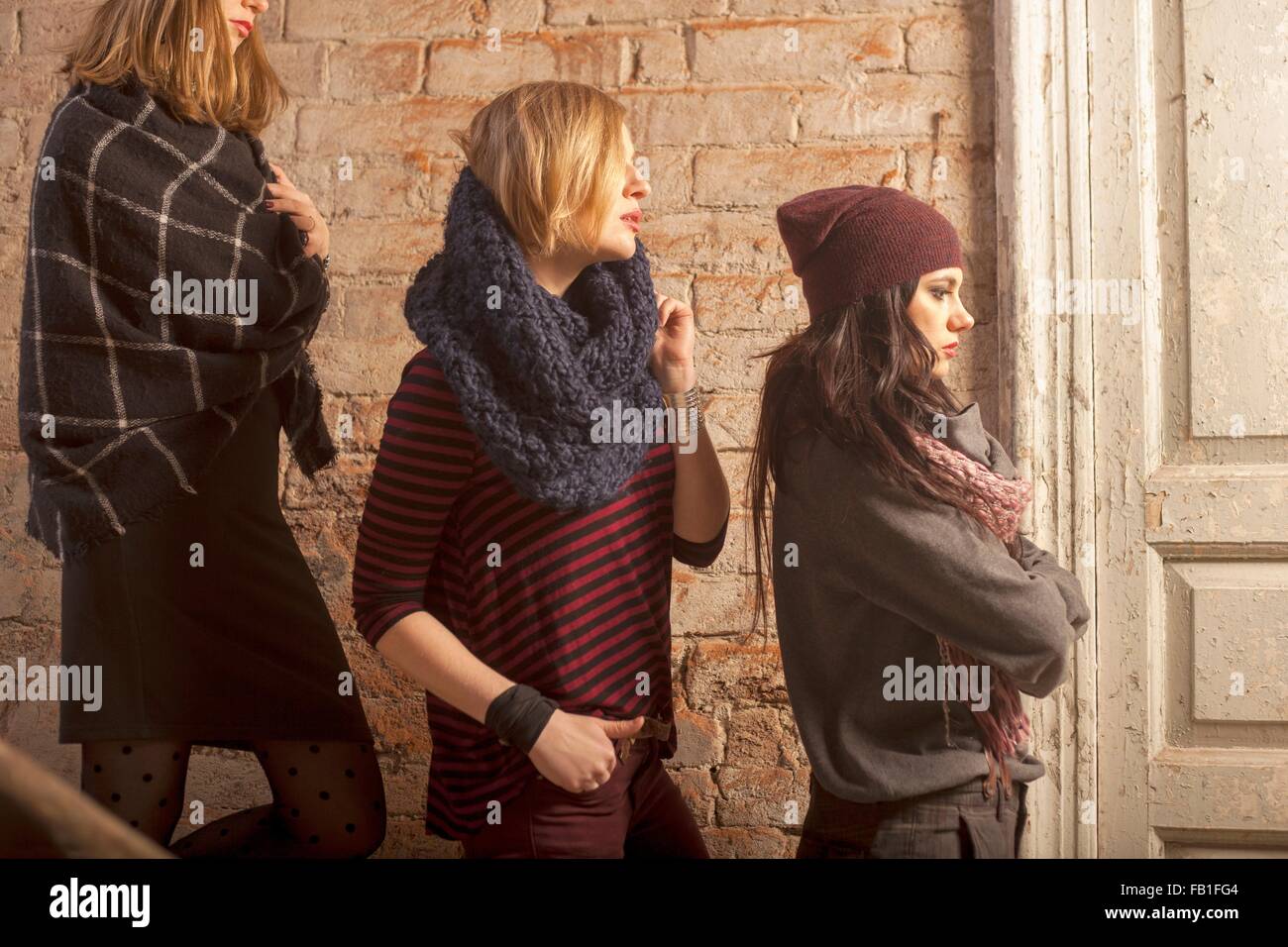 Side view of women wearing knitwear standing on stairs in front of brick wall looking away Stock Photo