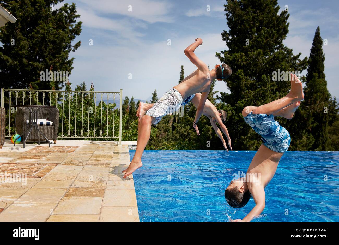 Three boys diving backward into apartment swimming pool Stock Photo