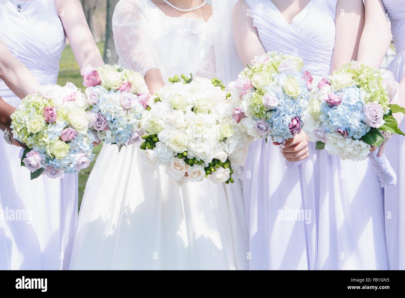 Cropped view of bride and bridesmaids side by side holding flower bouquets Stock Photo