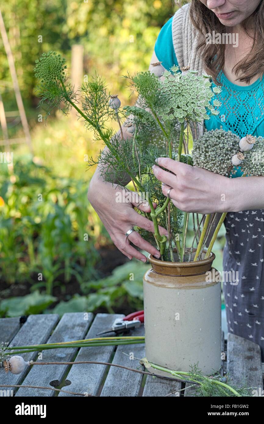 Mature woman arranging fresh ferns in jar at allotment Stock Photo