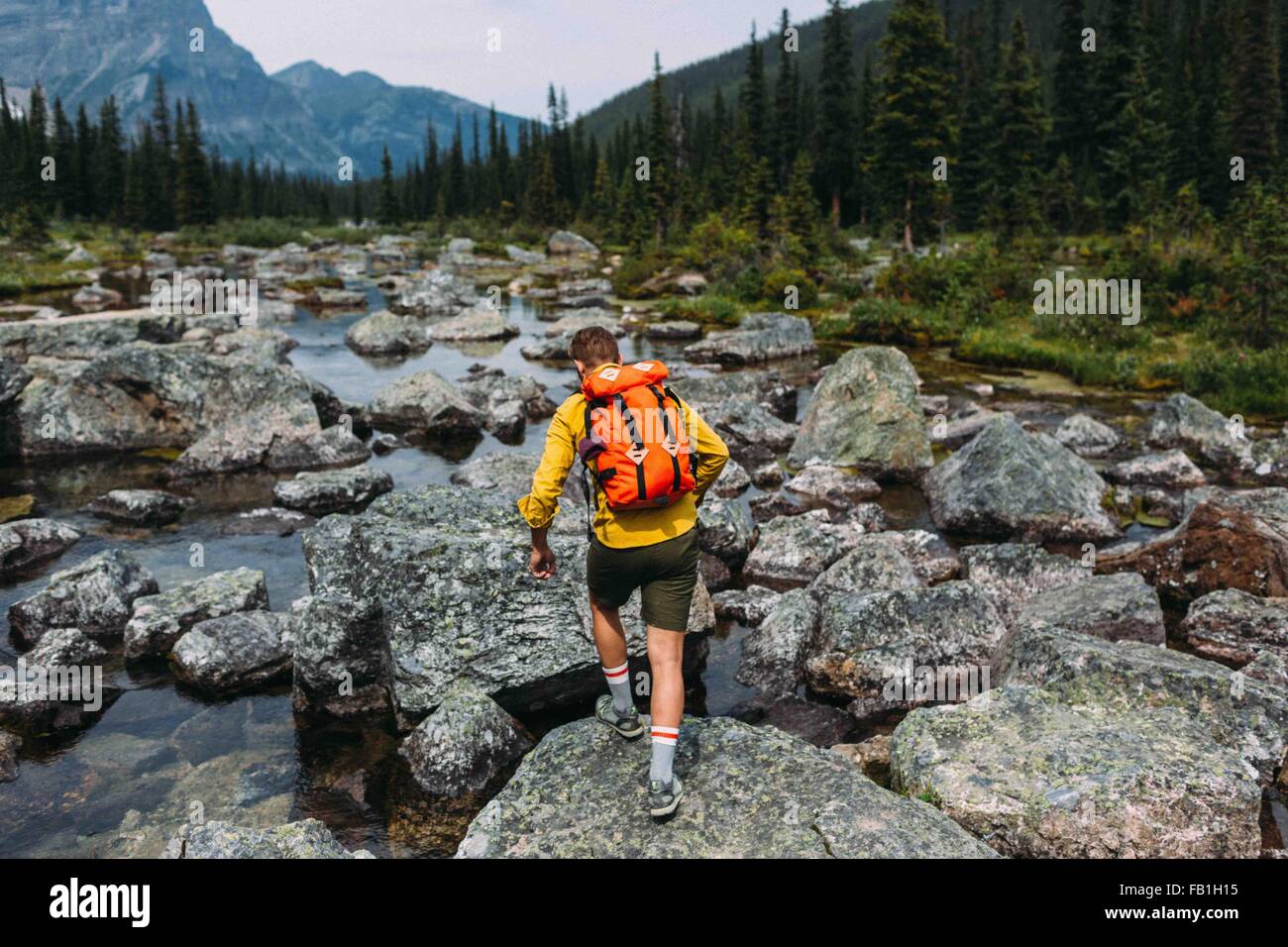 Rear view of mid adult man carrying backpack walking on rocky riverbed, Moraine lake, Banff National Park, Alberta Canada Stock Photo