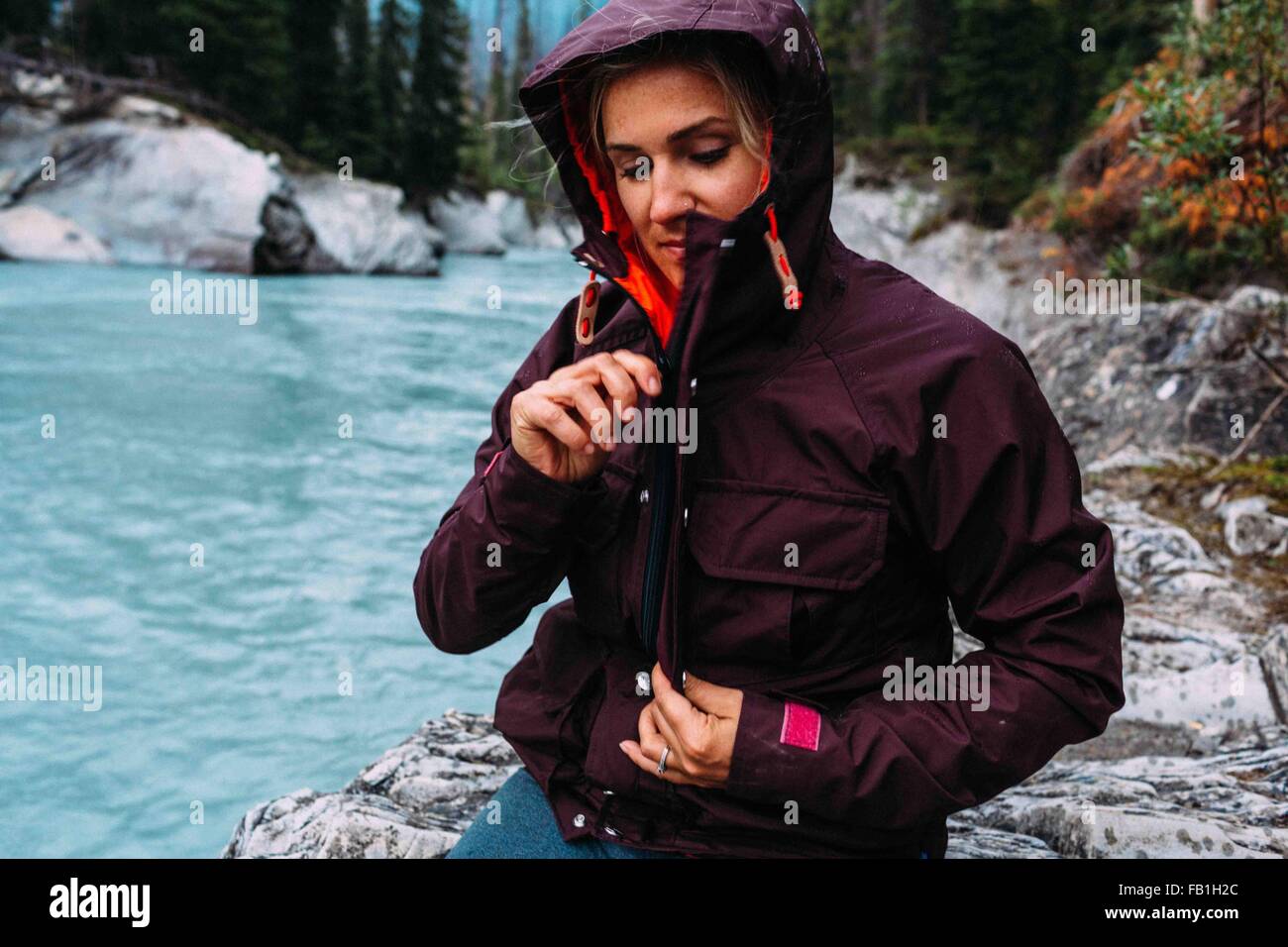 Mid adult woman by waters edge zipping up waterproof coat, Moraine lake, Banff National Park, Alberta Canada Stock Photo
