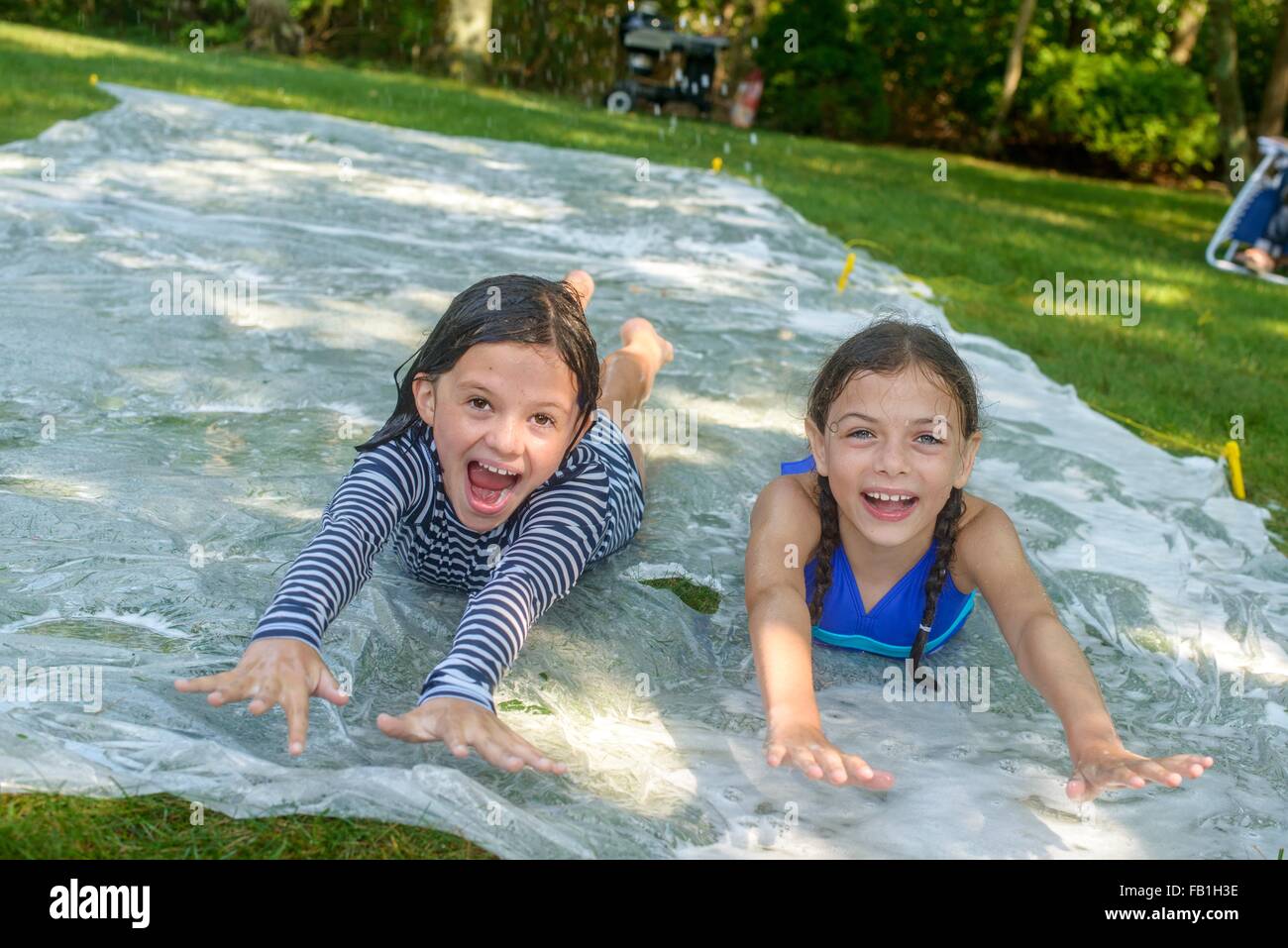 Two girls sliding on slip n slide water mat in garden Stock Photo