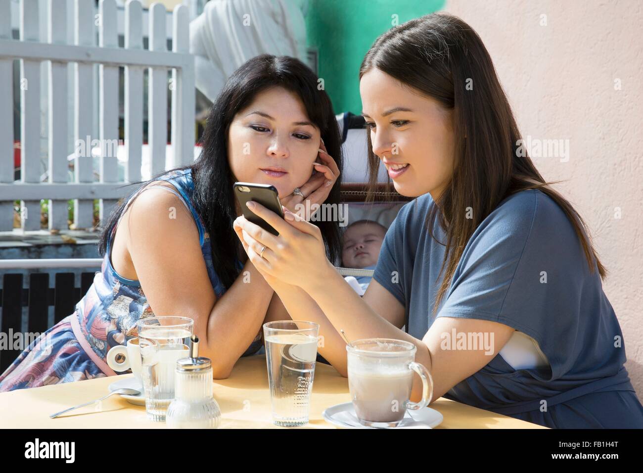 Young woman with mother and baby daughter reading smartphone text in cafe Stock Photo