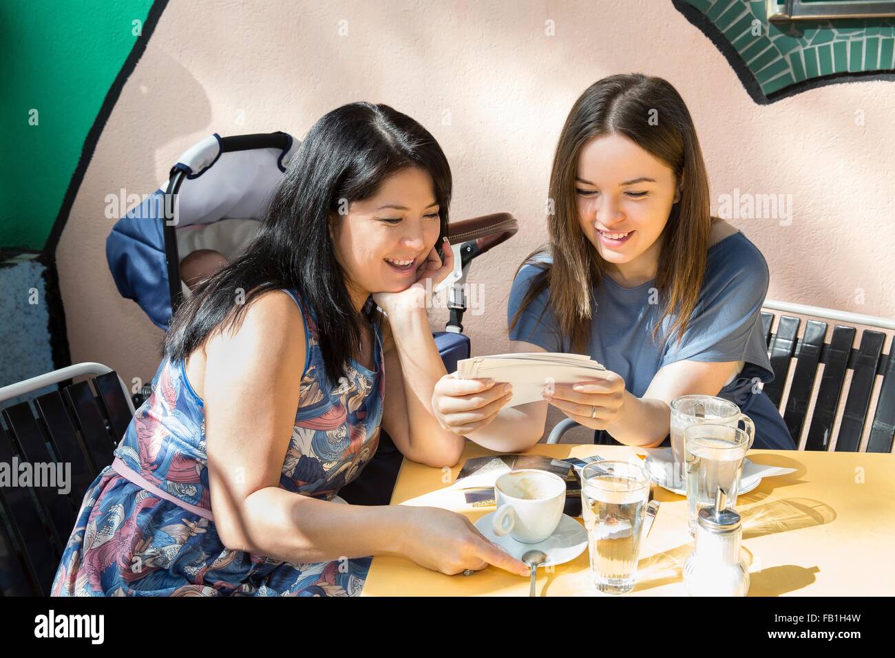 Young woman with mother and baby daughter looking at photographs at sidewalk cafe Stock Photo
