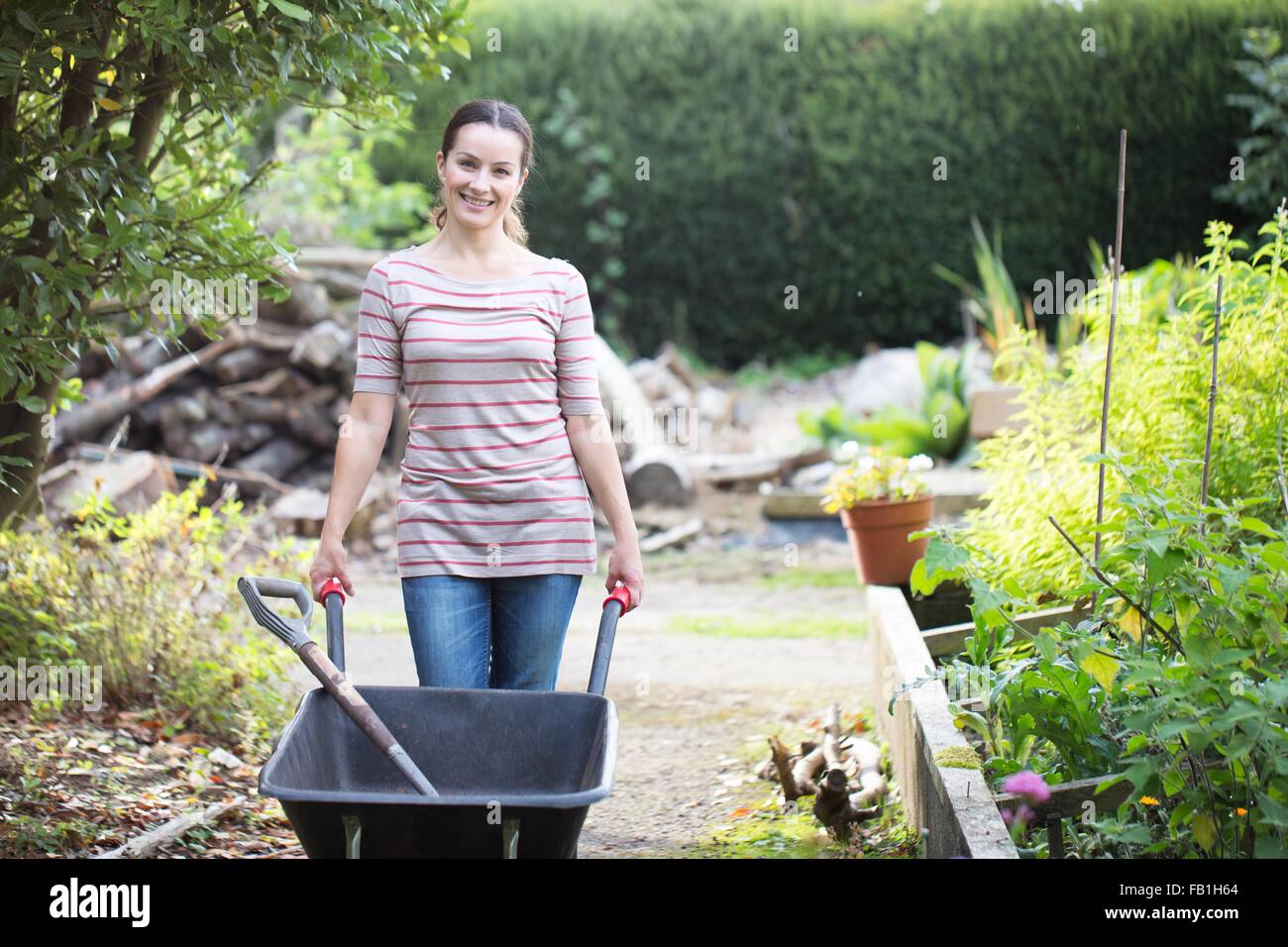 Portrait of female gardener pushing wheelbarrow in rustic organic ...