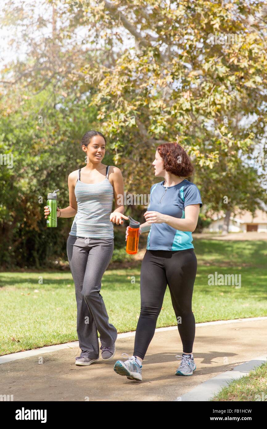 Young women out walking wearing sports clothing carrying water bottles talking Stock Photo