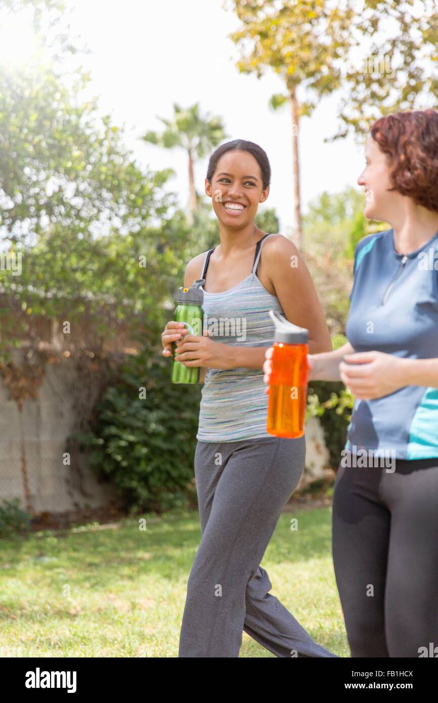Young women out walking wearing sports clothing carrying water bottles laughing Stock Photo