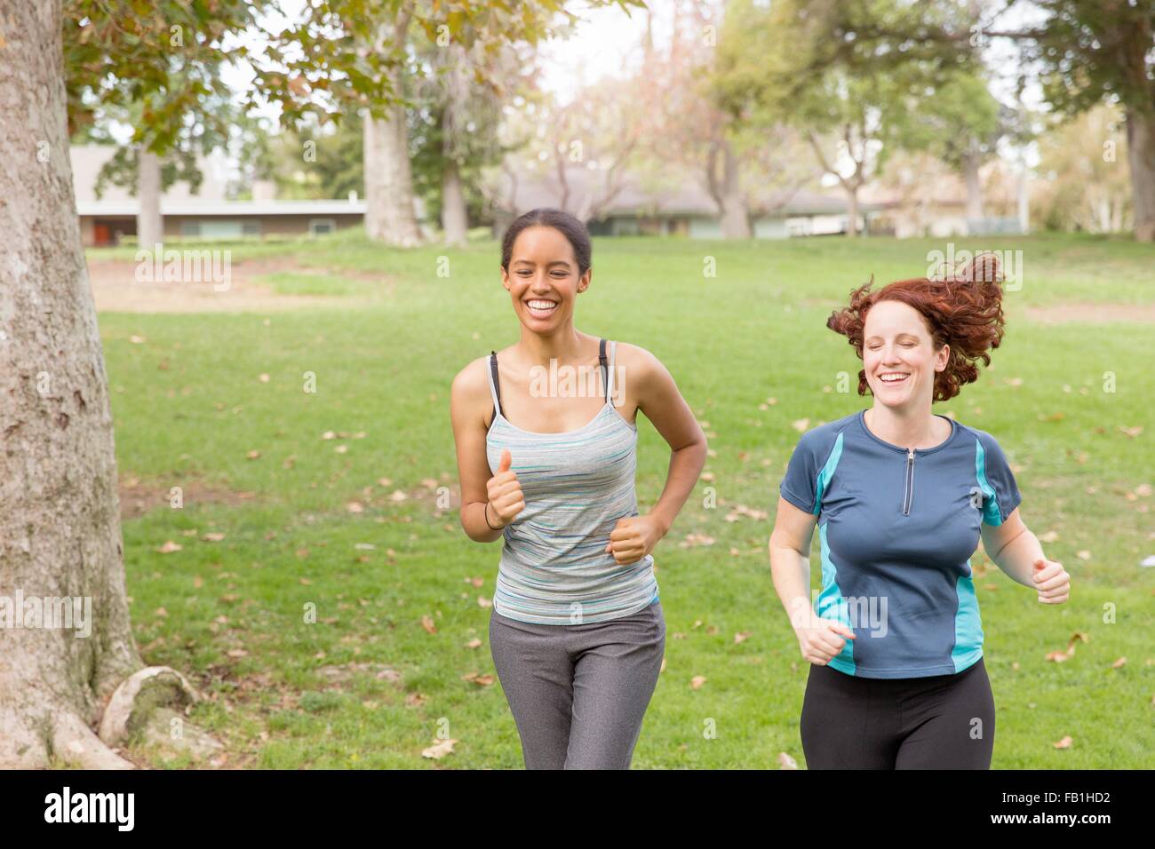 Full length front view of women wearing sport clothing running on grass smiling Stock Photo
