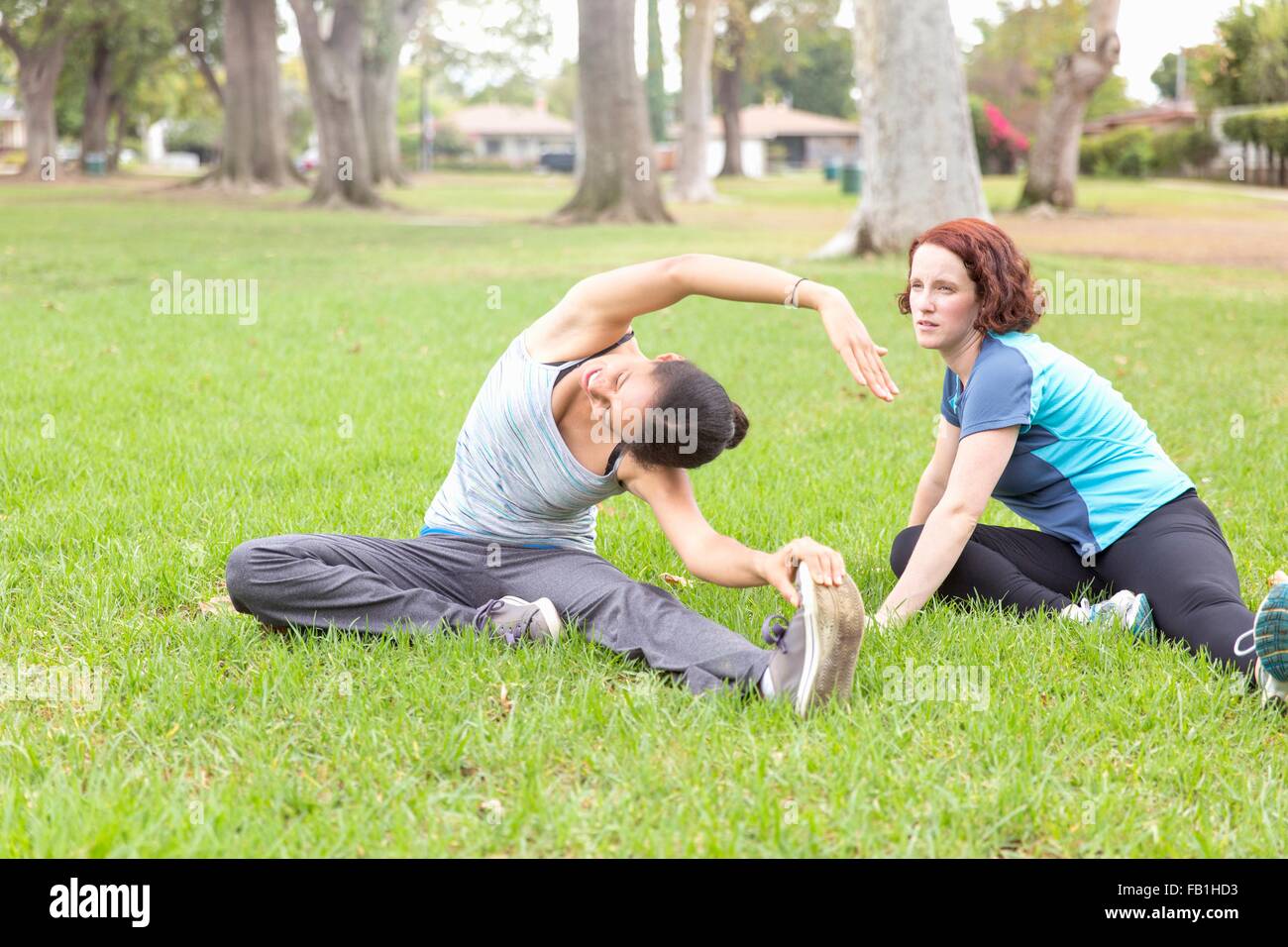 Young women wearing sports clothing sitting on grass stretching Stock Photo