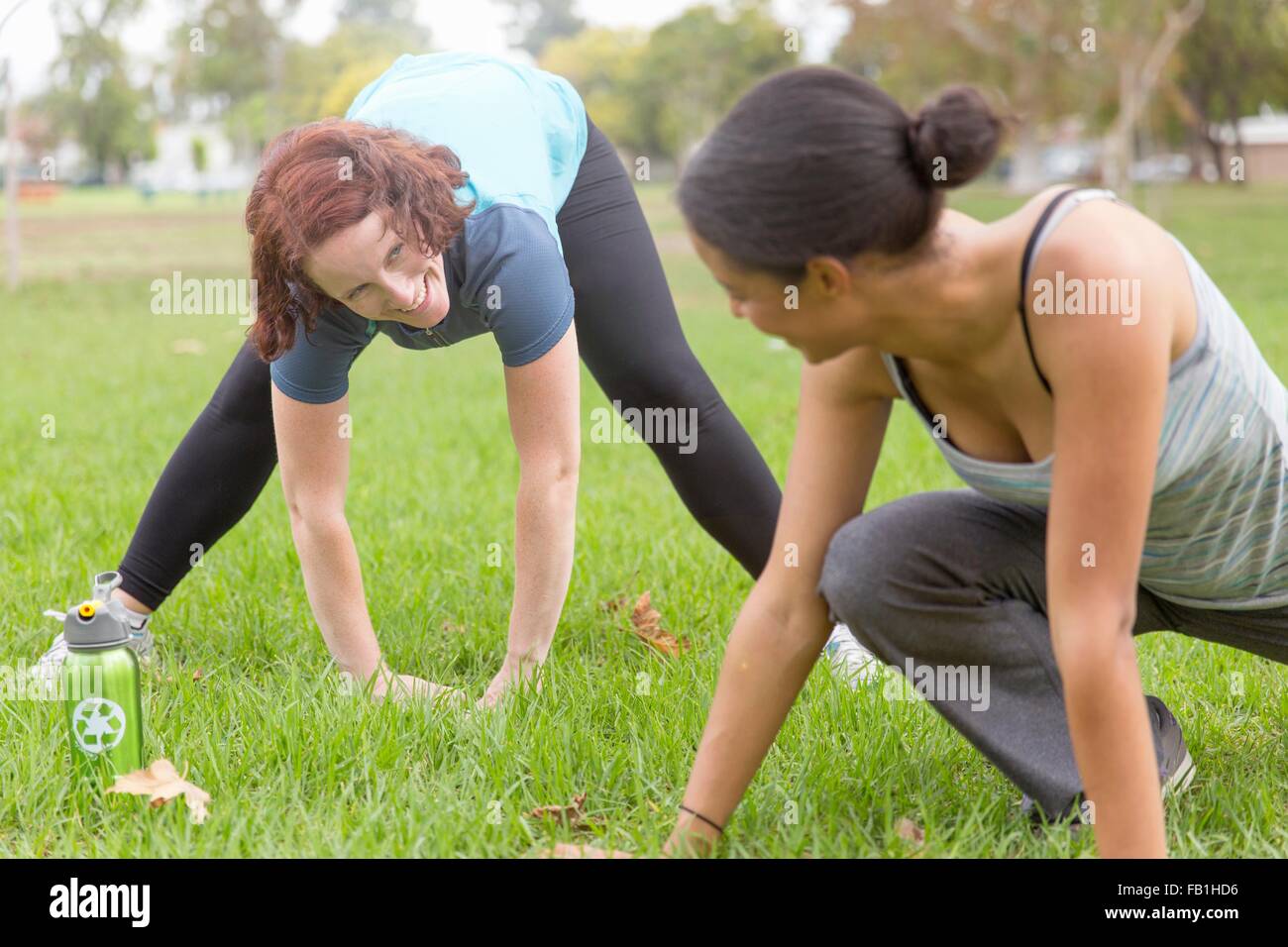 Young women wearing sports clothing on grass face to face bending over stretching Stock Photo