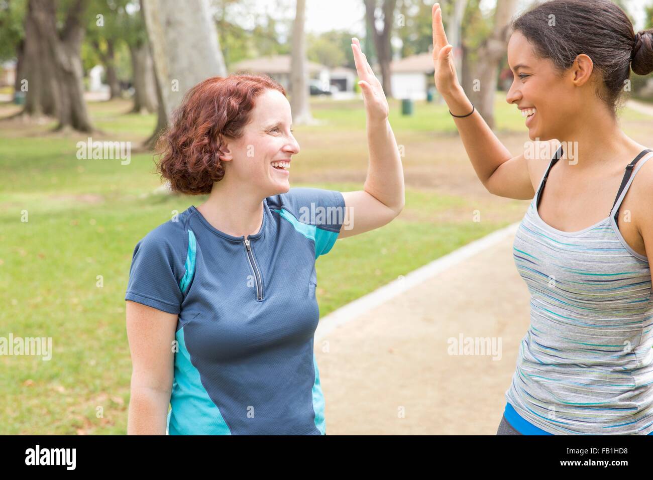 Young women wearing sports clothing face to face smiling doing high five Stock Photo