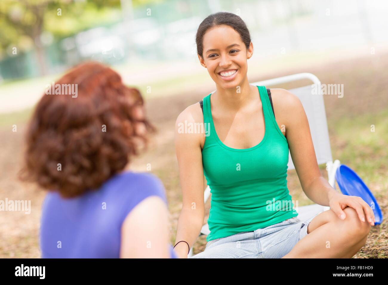 Young woman sitting crossed legs talking to friend, smiling Stock Photo