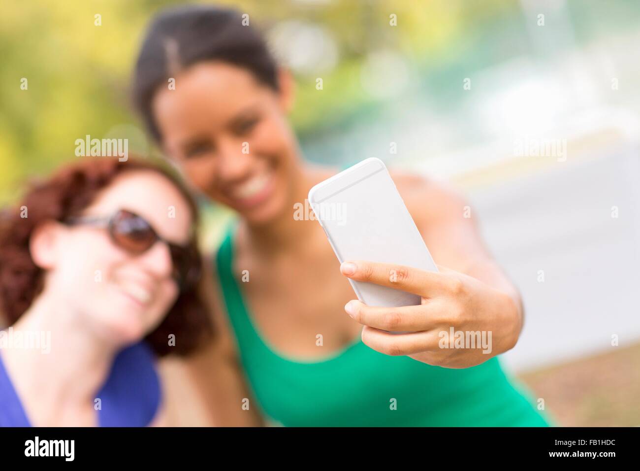 Young women using smartphone to take selfie smiling, focus on foreground Stock Photo