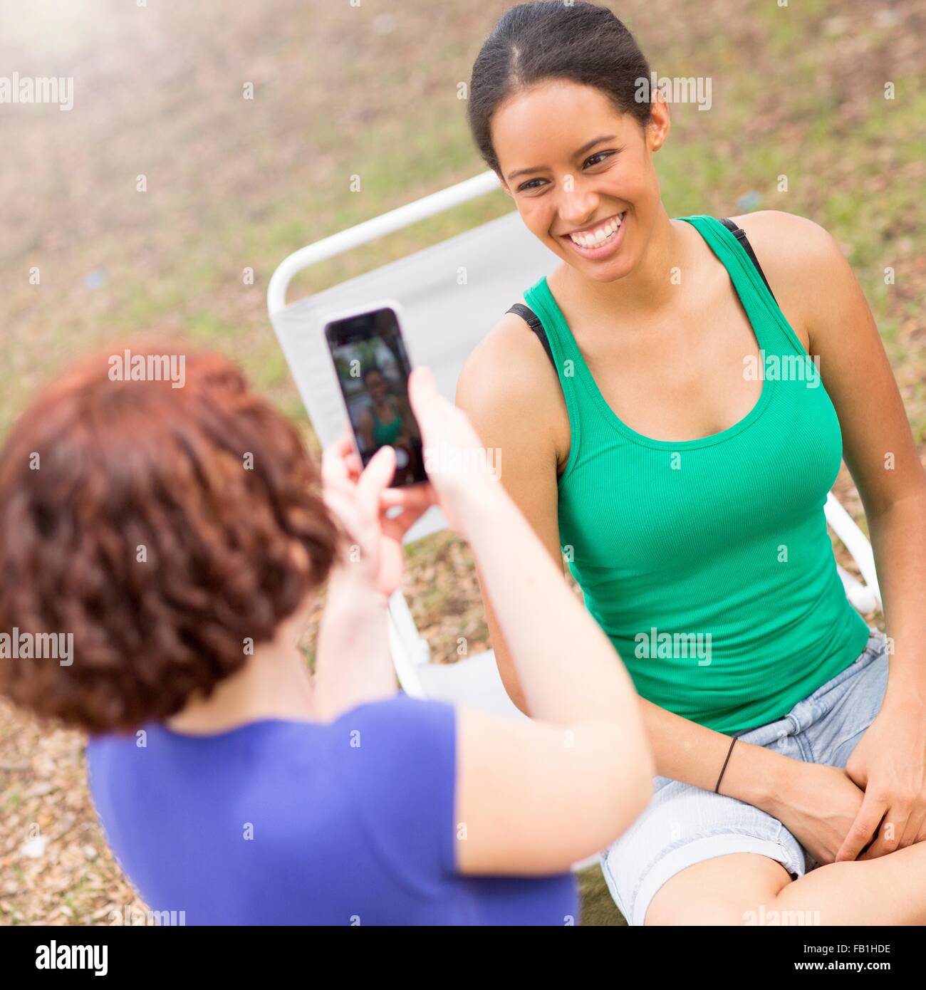 Young woman using smartphone to take photograph of smiling friend Stock Photo