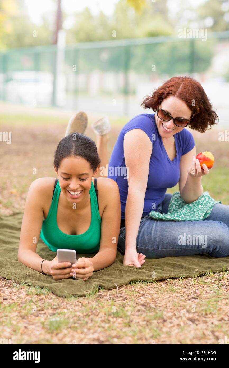 Young women on picnic blanket using smartphone looking down smiling Stock Photo