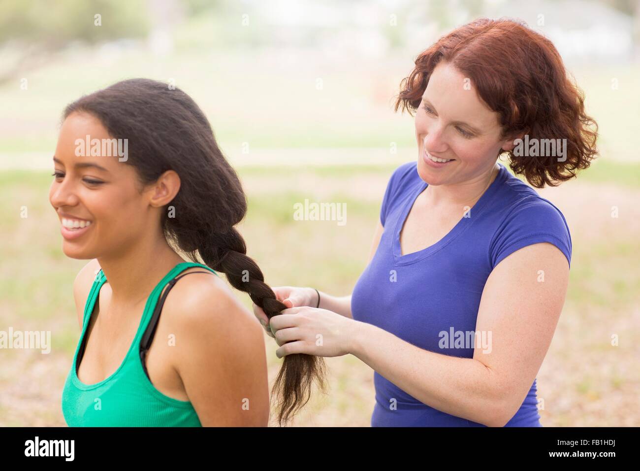 Young woman behind friend plaiting hair smiling Stock Photo