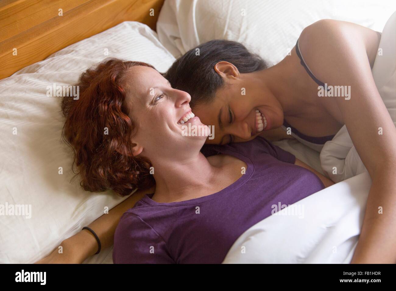 High angle view of lesbian couple lying in bed hugging, smiling Stock Photo