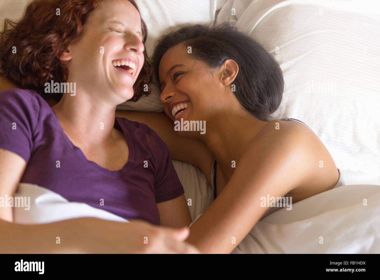High angle view of lesbian couple lying in bed hugging, laughing Stock Photo