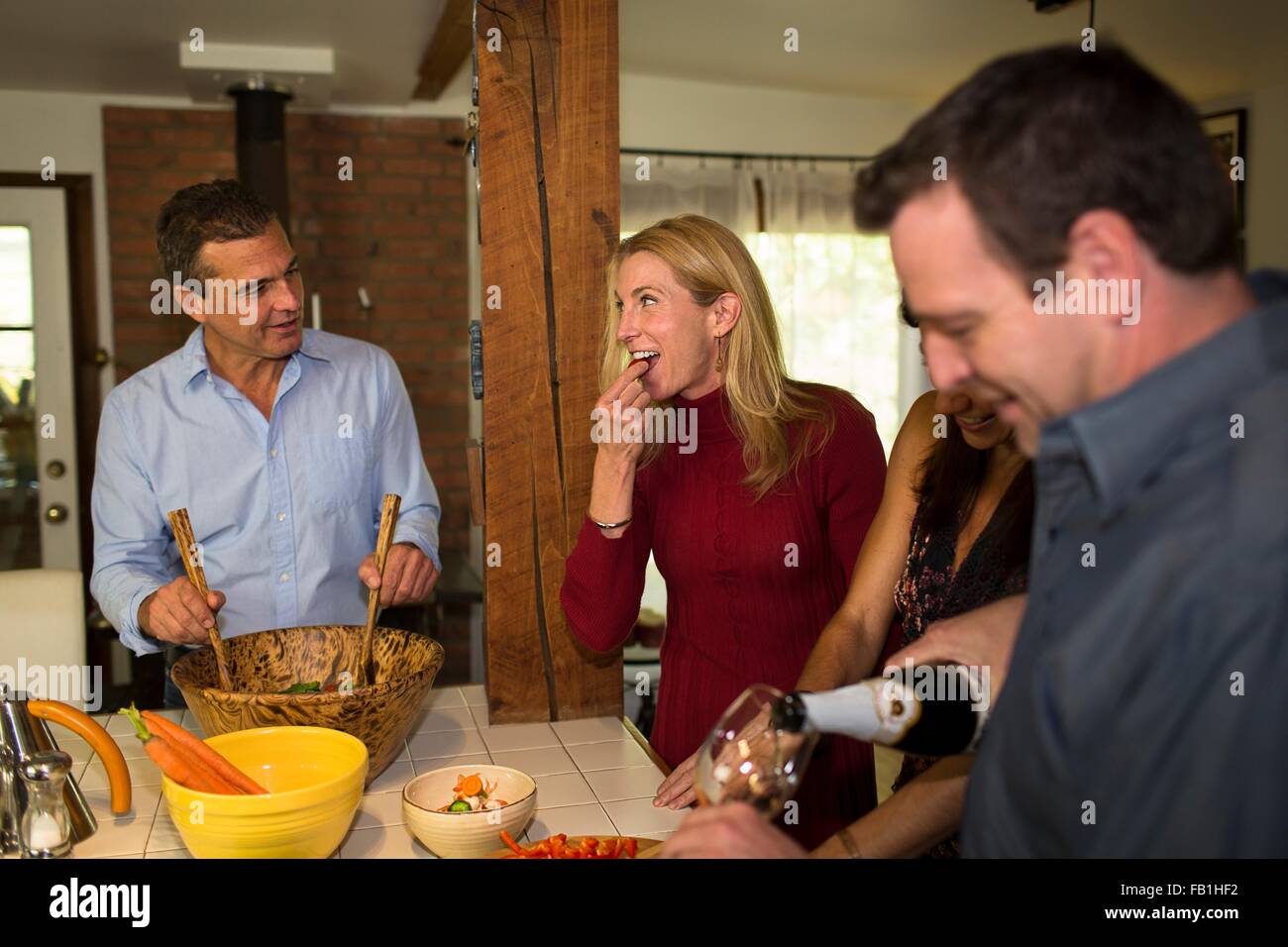 Two mature couples chatting and preparing food at dinner party Stock Photo