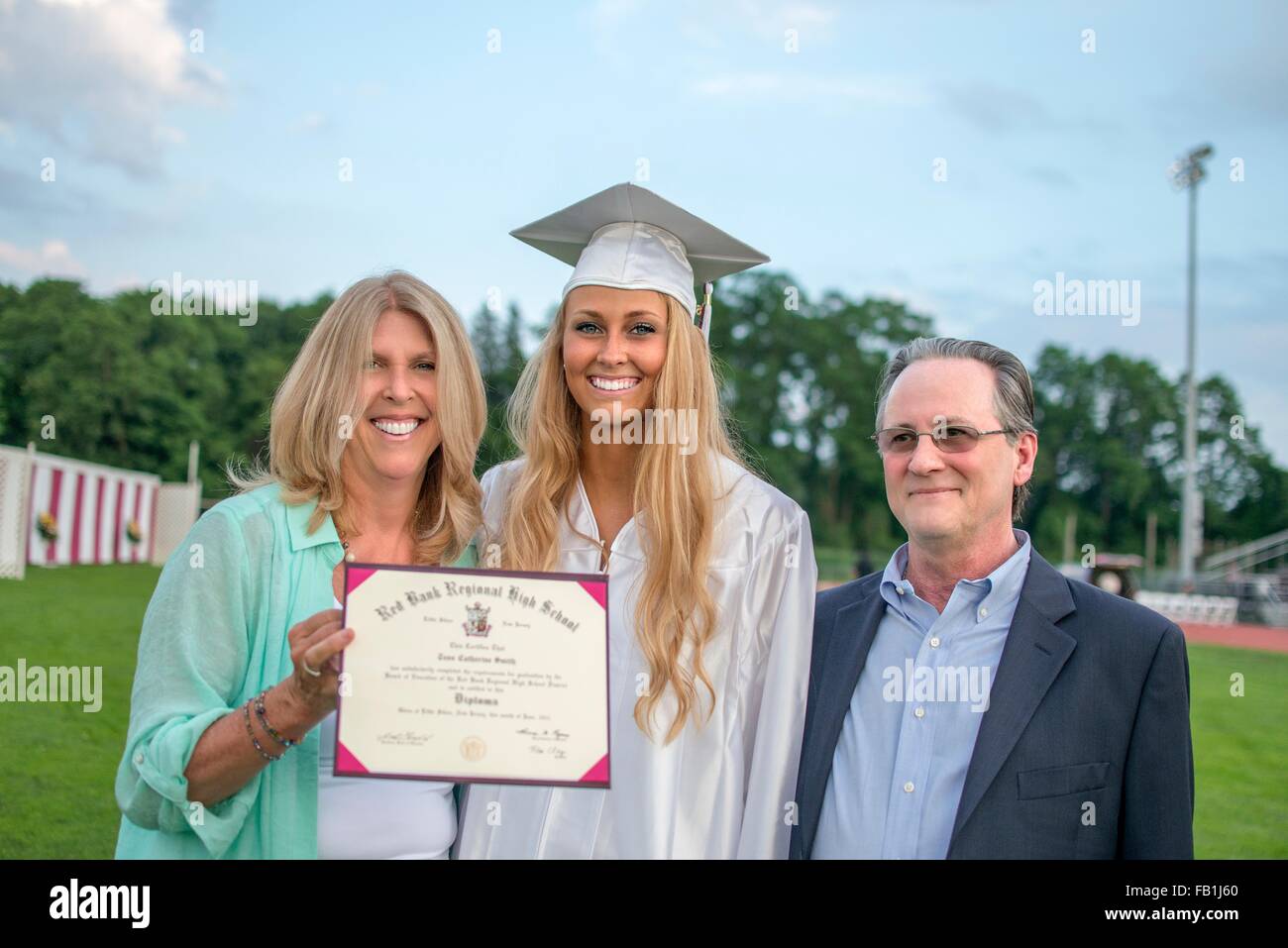 Portrait of young female graduate with parents at graduation ceremony Stock Photo
