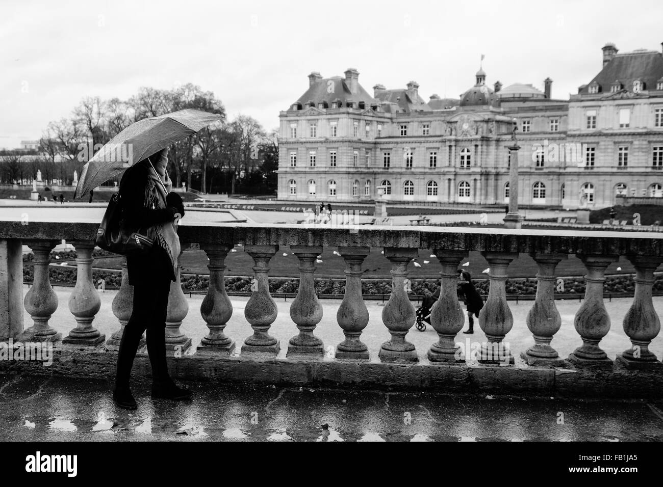 A beautiful young girl enjoys the view from under an umbrella on a rainy day at Jardin du Luxembourg in Paris, France. Stock Photo