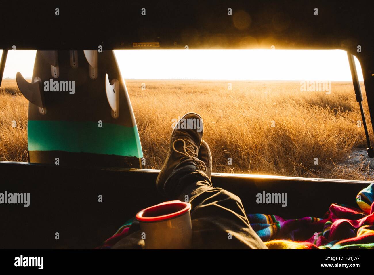 Male surfer with feet up in back of jeep at sunset, San Luis Obispo, California, USA Stock Photo