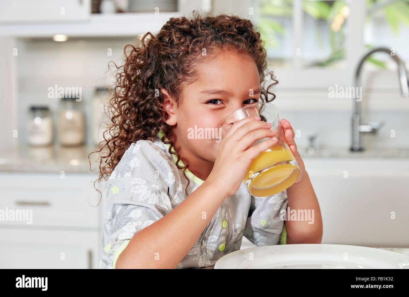 Girl at kitchen counter drinking orange juice looking at camera Stock Photo