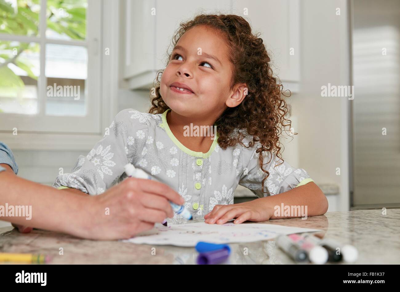 Girl at kitchen counter using felt tip pen to draw picture, looking up smiling Stock Photo