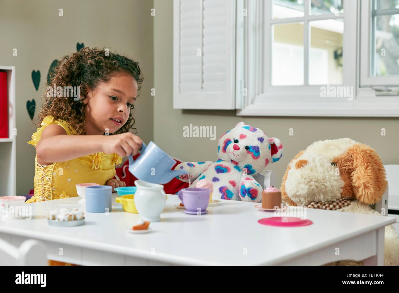 Girl in playroom sitting at table serving tea from toy tea set to ... Girl in playroom sitting at table serving tea from toy tea set to ...