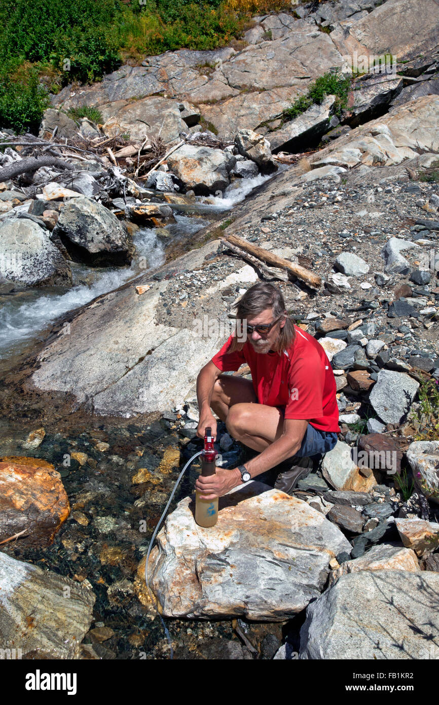WASHINGTON - Hiker using a pump to purify water from a small stream in the Napeequa River Valley in the Glacier Peak Wilderness. Stock Photo