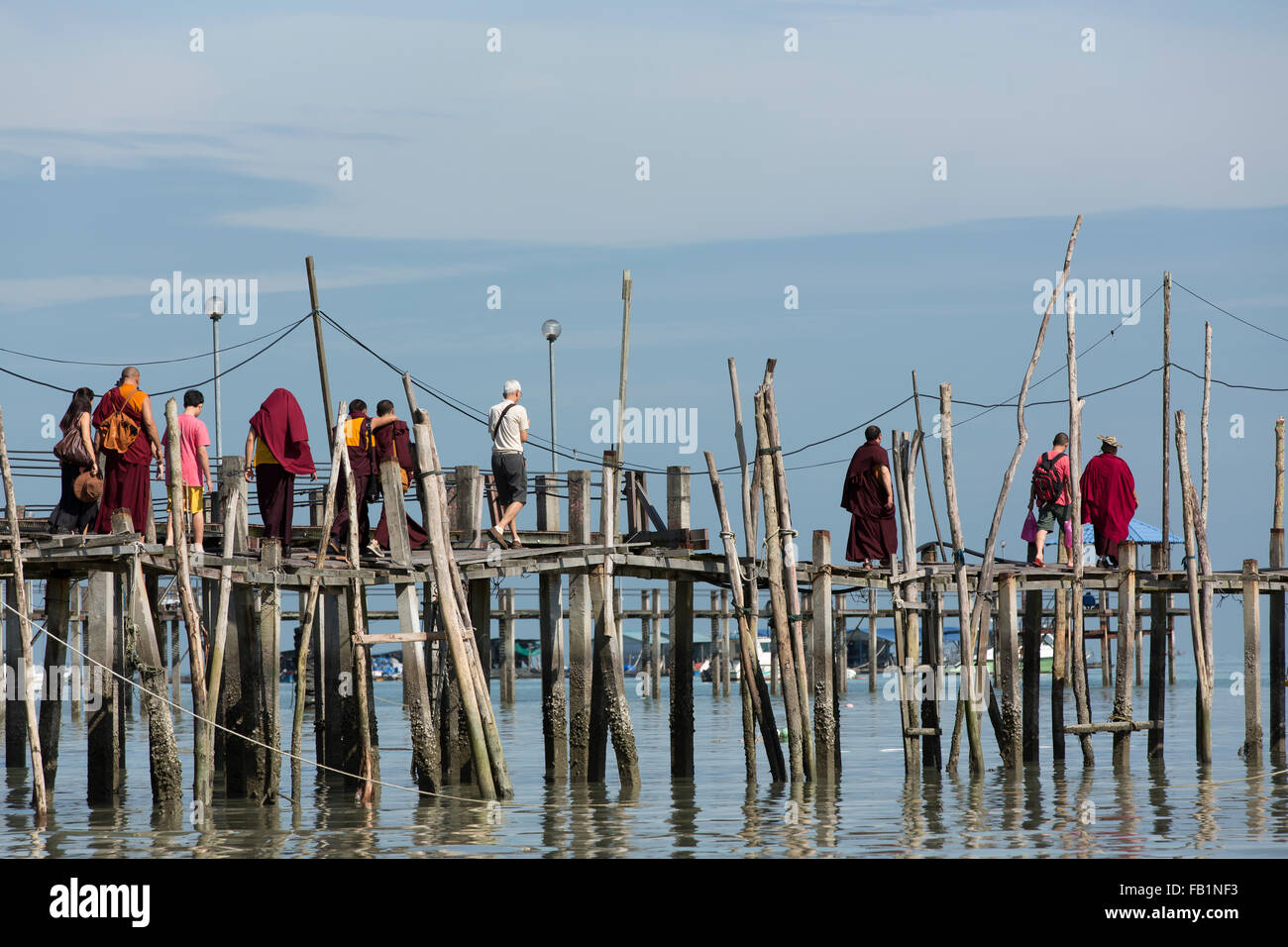 Buddhist pilgrims walking along a wooden jetty at Teluk Bahang Penang to catch a ferry on their way to complete their journey. Stock Photo