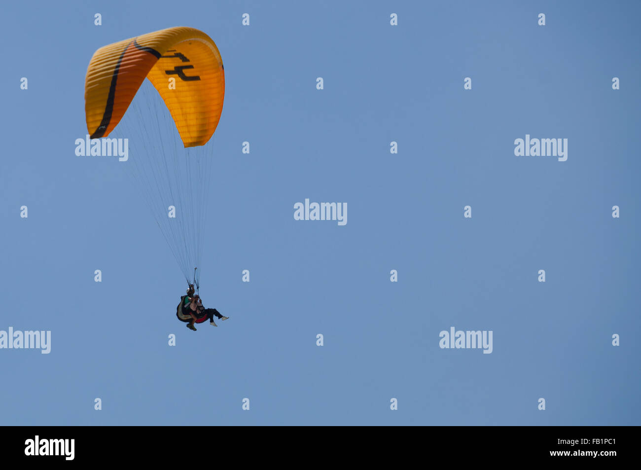 Paraglide tandem with yellow parachute in the blue sky Stock Photo